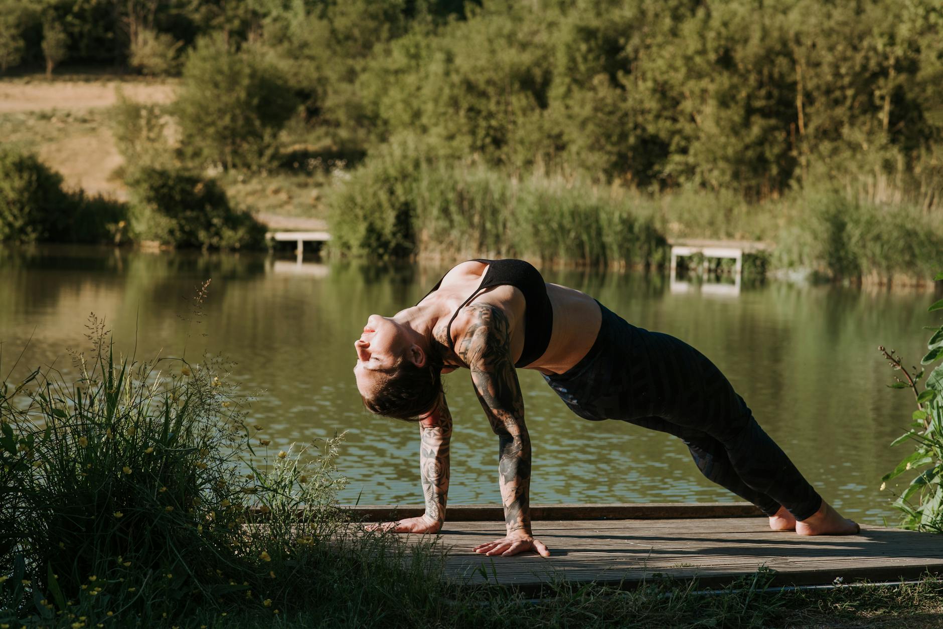 Woman practicing yoga on a dock with a beautiful lake behind.